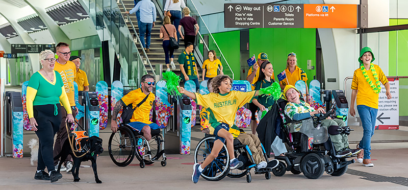 Adults and children (including some in wheelchairs and with guide dogs) at a train station.