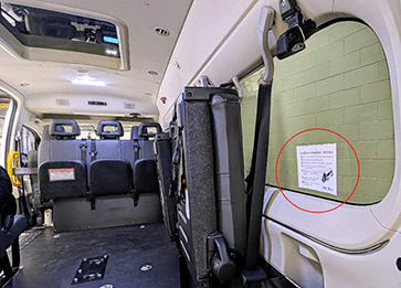 View of the inside a wheelchair taxi from the back door and showing a sticker placed on the bottom right quadrant of the rear back window on the interior right-hand side of the vehicle.