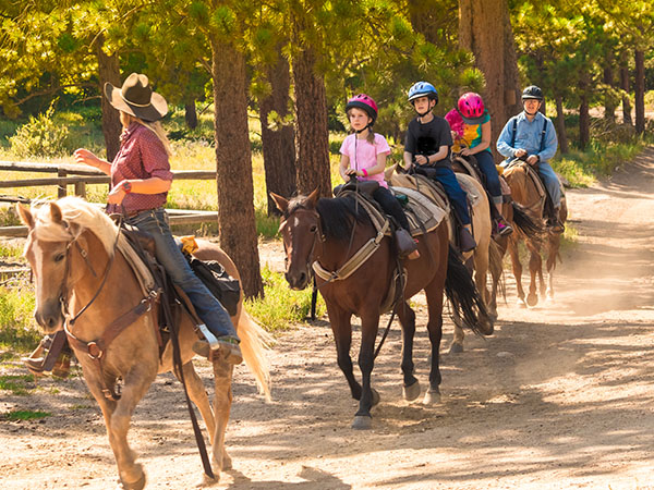 An adult on horseback leading several children on horseback