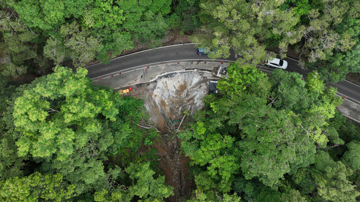 Aerial image of Kuranda Range Road, showing large green trees and a curved road which has temporary stabilisation repairs following a major landslip on the side of the road. 