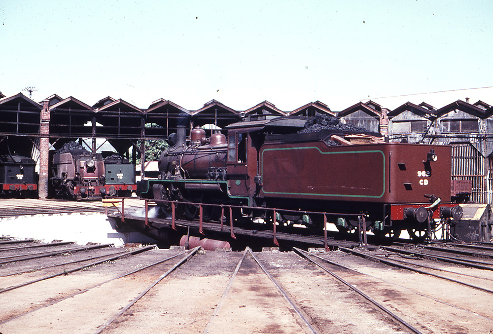 1966 photo of a steam train on the Roundhouse turntable with three steam trains in the background sheds.
