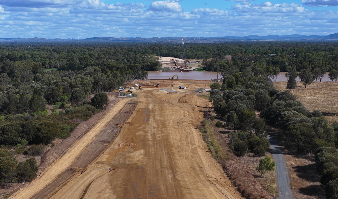 Aerial view of a cleared road with trees on either side of the road and a cloudy sky in the background. 