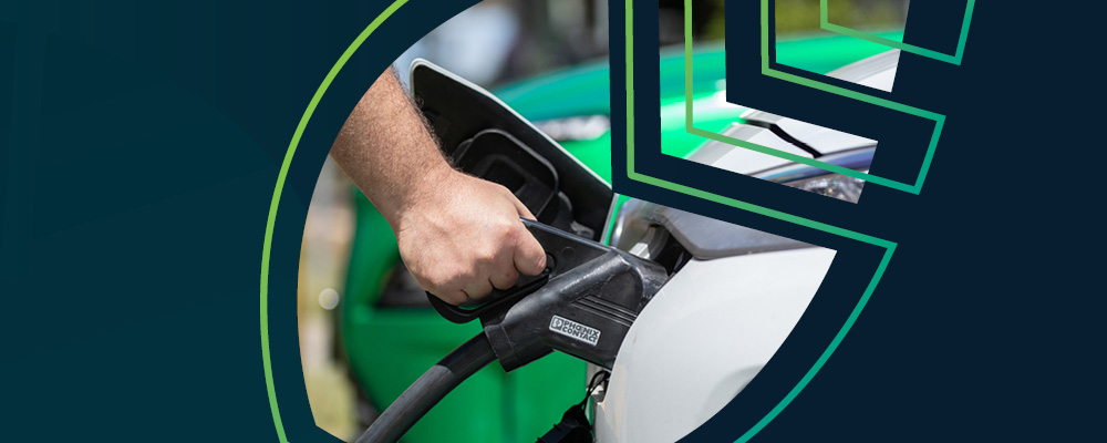 A hand holding a black electric vehicle charging handle. The image is set against a navy blue background.