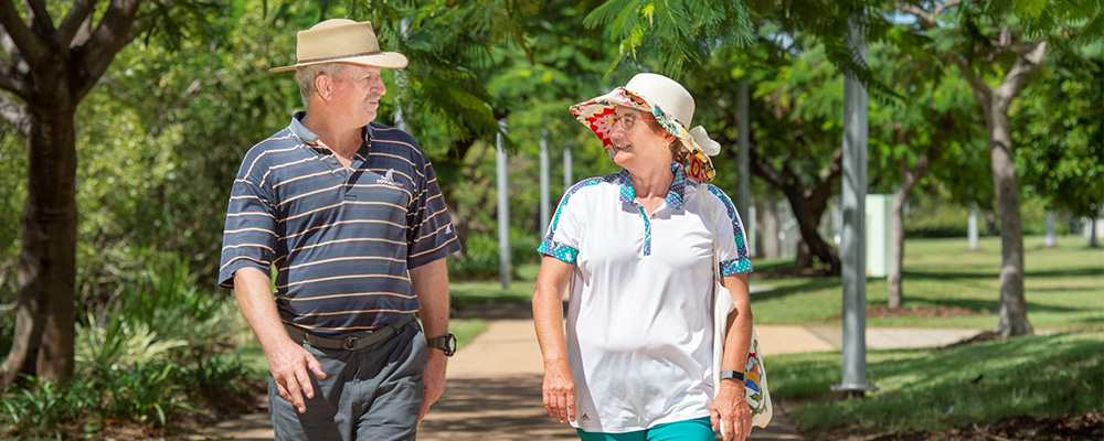 A man and woman in hats looking at each other while they walk along on a path.