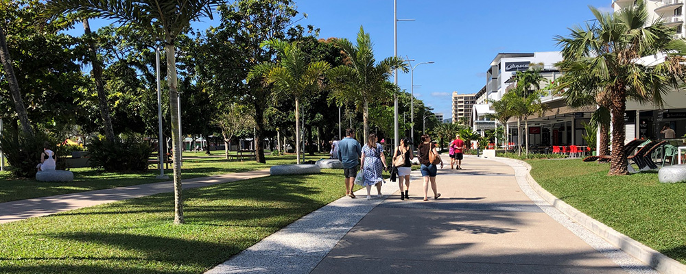 A group of people walking on a path next to palm trees and grass. 