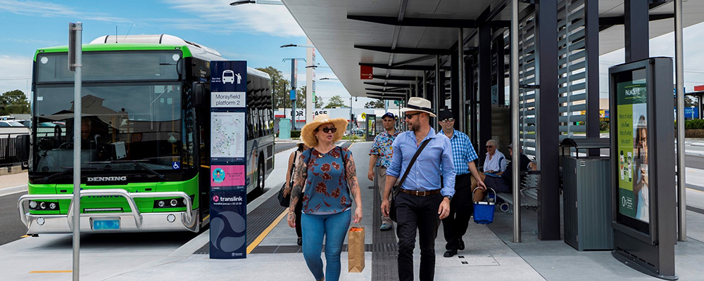 People walking at bus station at Morayfield carrying bags and talking. 