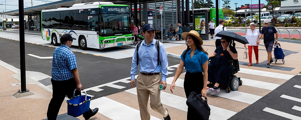 People walking and moving with the help of a wheelchair on a raised zebra crossing at a bus station. 